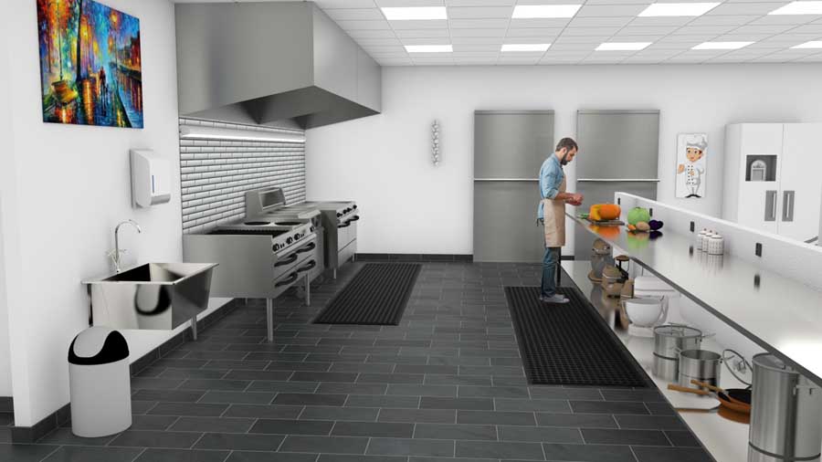 På bilde ser du gulvfliser på et kjøkken i et kantinekjøkken og en manm der står og jobber på avlastingsmatter.